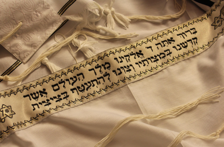 A traditional Jewish tallit (prayer shawl) with blue and white stripes and tzitzit fringes